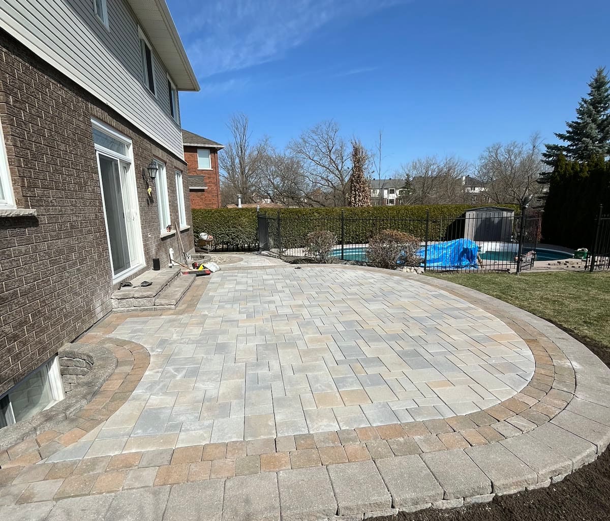 Backyard interlock patio with pool border and curved seat wall in Ottawa